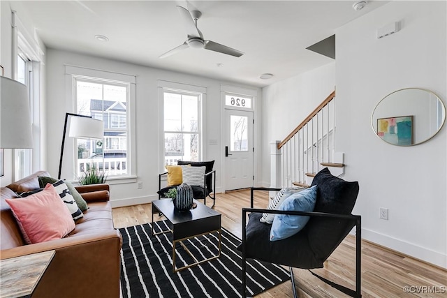 living area with light wood-style floors, ceiling fan, baseboards, and stairs