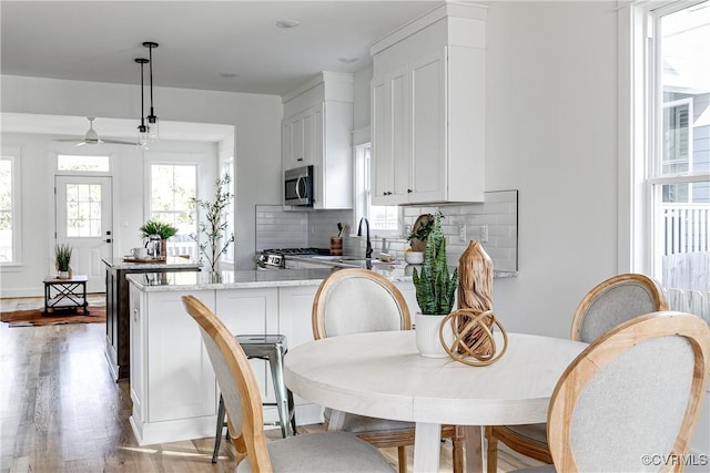 kitchen with light stone counters, white cabinetry, a healthy amount of sunlight, stainless steel microwave, and pendant lighting