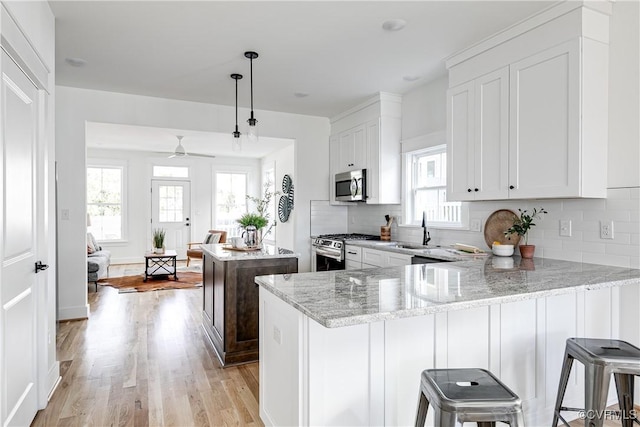 kitchen with stainless steel appliances, white cabinetry, a peninsula, and light stone countertops