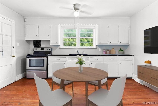 kitchen with dark countertops, electric stove, wood finished floors, white cabinets, and a sink