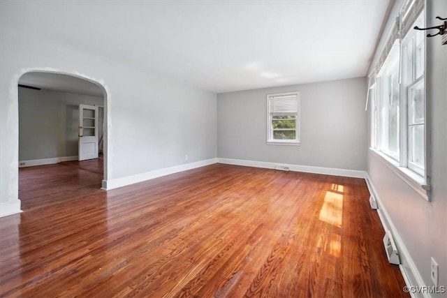 spare room featuring baseboards, arched walkways, and wood finished floors