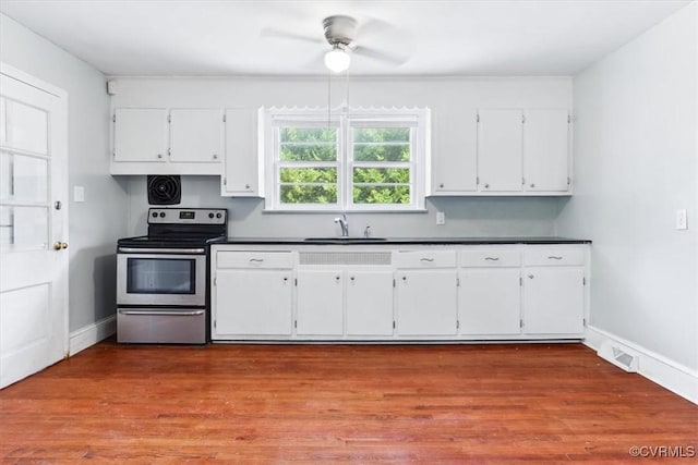 kitchen featuring dark countertops, visible vents, stainless steel range with electric stovetop, white cabinetry, and a sink