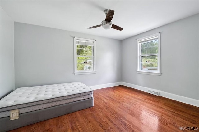 bedroom with visible vents, multiple windows, baseboards, and wood finished floors