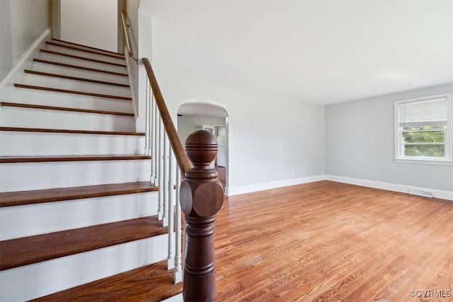 stairway featuring arched walkways, visible vents, baseboards, and wood finished floors