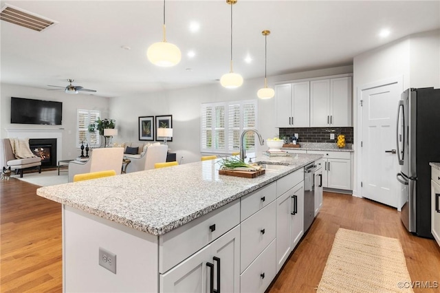 kitchen with a ceiling fan, visible vents, a warm lit fireplace, a sink, and stainless steel appliances