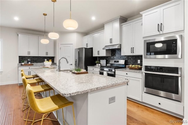 kitchen with under cabinet range hood, a center island with sink, a kitchen bar, appliances with stainless steel finishes, and a sink