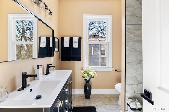 full bathroom featuring double vanity, baseboards, toilet, and a sink