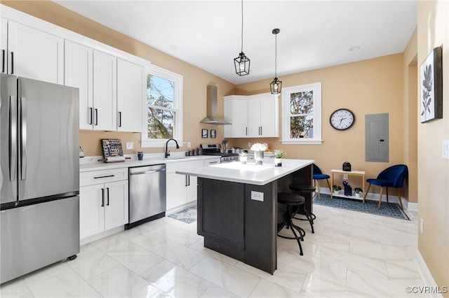 kitchen featuring a kitchen island, appliances with stainless steel finishes, decorative light fixtures, light countertops, and wall chimney range hood