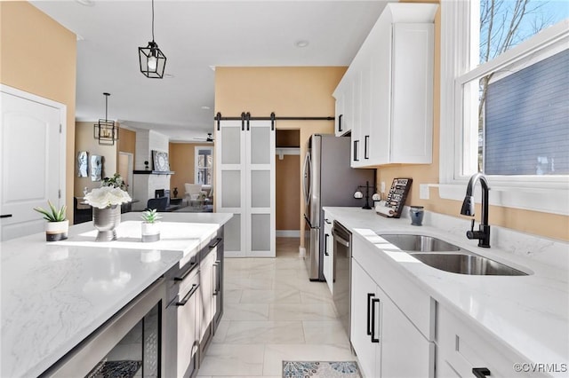 kitchen with a barn door, white cabinets, light stone counters, pendant lighting, and a sink