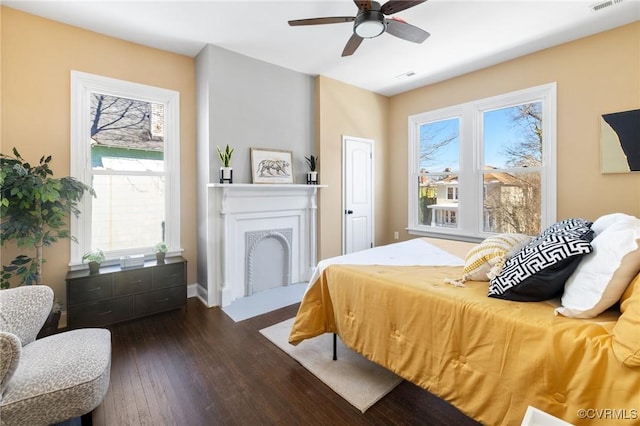 bedroom featuring baseboards, visible vents, a ceiling fan, a fireplace with flush hearth, and dark wood-style flooring