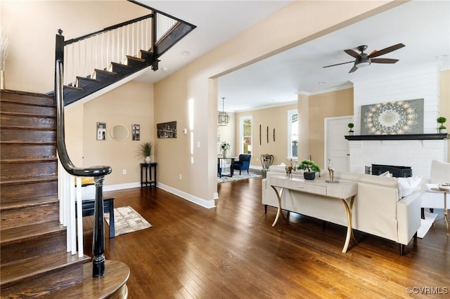 living area featuring dark wood-style floors, ornamental molding, a brick fireplace, baseboards, and stairs