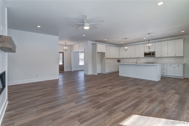 kitchen with white cabinets, an island with sink, stainless steel microwave, a fireplace, and pendant lighting