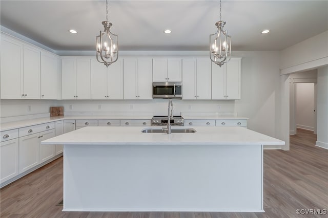 kitchen featuring light countertops, stainless steel microwave, an island with sink, and white cabinetry