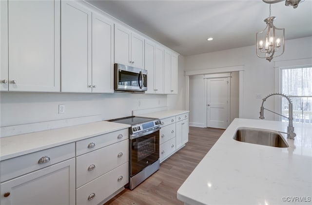 kitchen with stainless steel appliances, a sink, white cabinetry, light wood-style floors, and pendant lighting