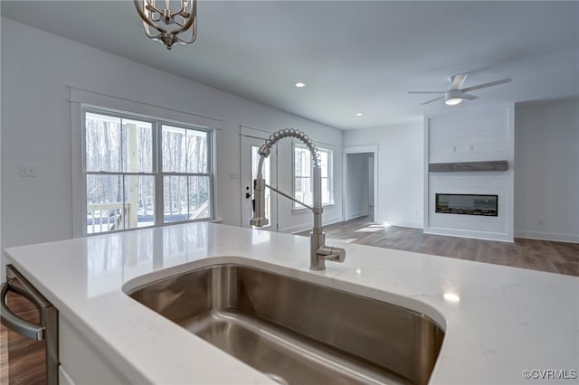 kitchen with a large fireplace, dark wood-style flooring, a sink, stainless steel dishwasher, and recessed lighting