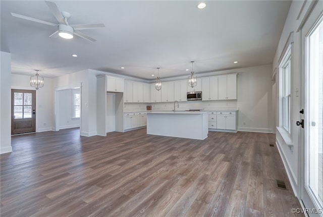 kitchen featuring light countertops, a kitchen island with sink, stainless steel microwave, and white cabinetry