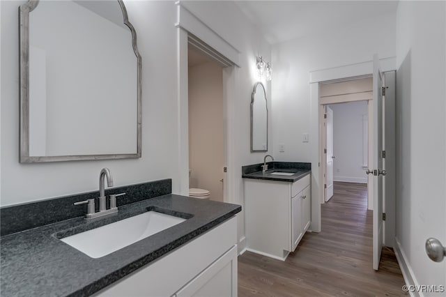 bathroom featuring wood finished floors, two vanities, a sink, and baseboards