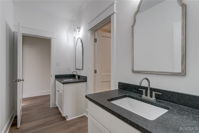 bathroom featuring wood finished floors, two vanities, a sink, and baseboards