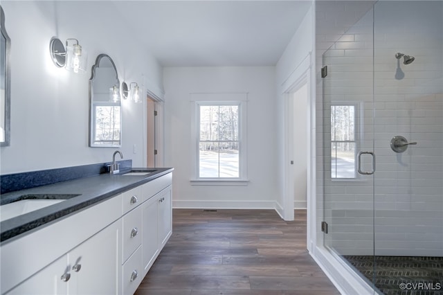 full bath with double vanity, a stall shower, a sink, wood finished floors, and baseboards