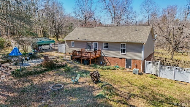 rear view of property with a lawn, a fire pit, a deck, and fence