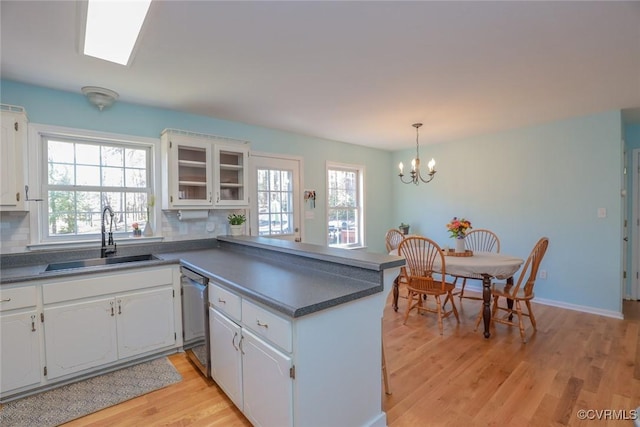 kitchen featuring a sink, stainless steel dishwasher, a peninsula, and white cabinetry