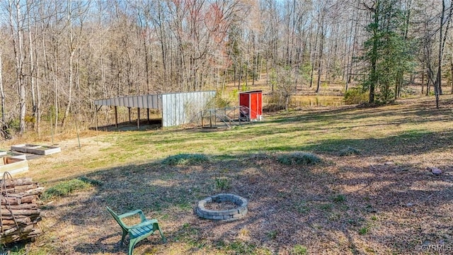 view of yard featuring an outbuilding, a fire pit, and a forest view