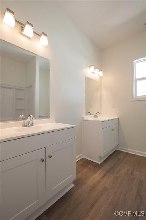 bathroom featuring two vanities, a sink, baseboards, and wood finished floors