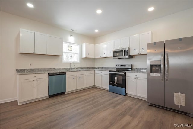 kitchen featuring stainless steel appliances, recessed lighting, white cabinets, a sink, and wood finished floors