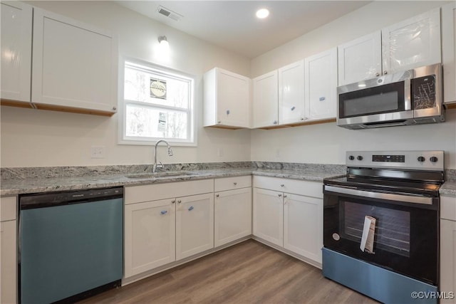 kitchen with stainless steel appliances, wood finished floors, a sink, visible vents, and white cabinets