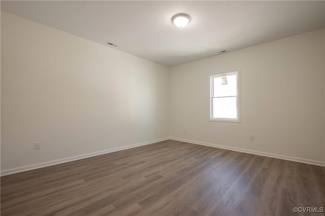 empty room featuring visible vents, baseboards, and dark wood finished floors