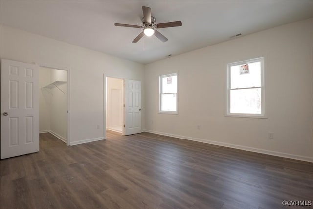 unfurnished bedroom with dark wood-type flooring, visible vents, a spacious closet, and baseboards