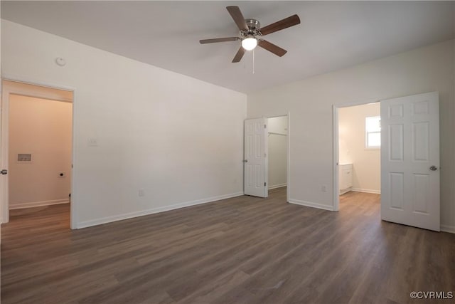 unfurnished bedroom with a walk in closet, dark wood-style flooring, a closet, ensuite bathroom, and baseboards