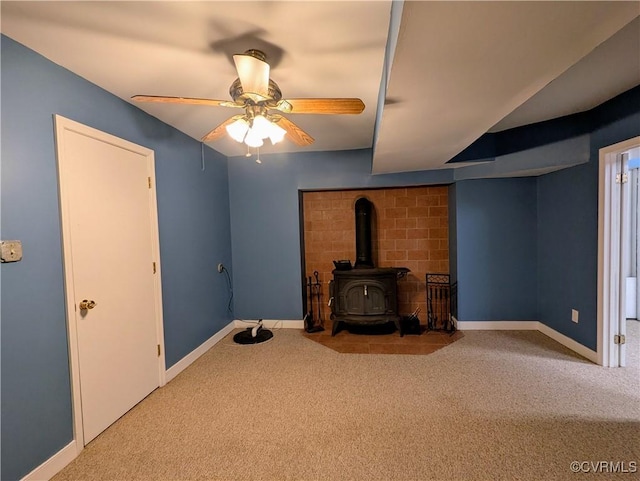 unfurnished living room with a ceiling fan, a wood stove, carpet, and baseboards