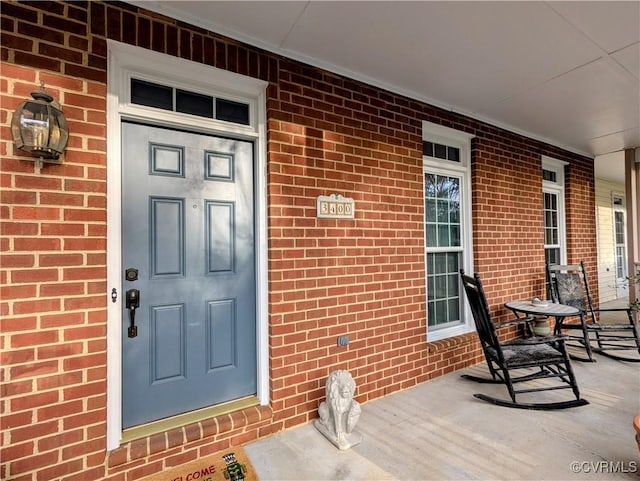 doorway to property featuring a porch and brick siding