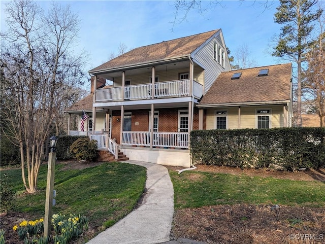 view of front of home featuring a front yard, a balcony, roof with shingles, a porch, and brick siding