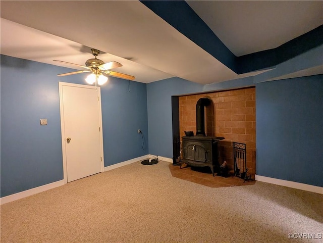 carpeted living area with a wood stove, baseboards, and ceiling fan