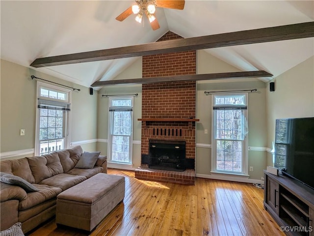 living area featuring vaulted ceiling with beams, a healthy amount of sunlight, hardwood / wood-style floors, and a fireplace