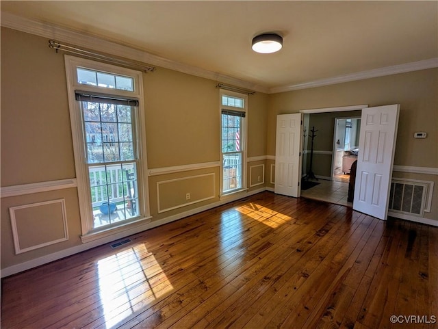 unfurnished room with a decorative wall, visible vents, dark wood-style flooring, and ornamental molding