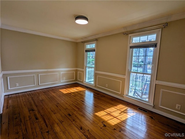 empty room featuring visible vents, hardwood / wood-style floors, crown molding, and a decorative wall