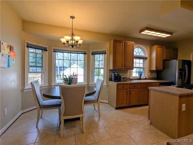 kitchen featuring baseboards, an inviting chandelier, a sink, hanging light fixtures, and stainless steel refrigerator with ice dispenser