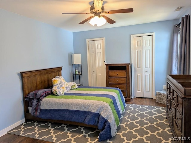 bedroom featuring visible vents, two closets, wood finished floors, baseboards, and ceiling fan