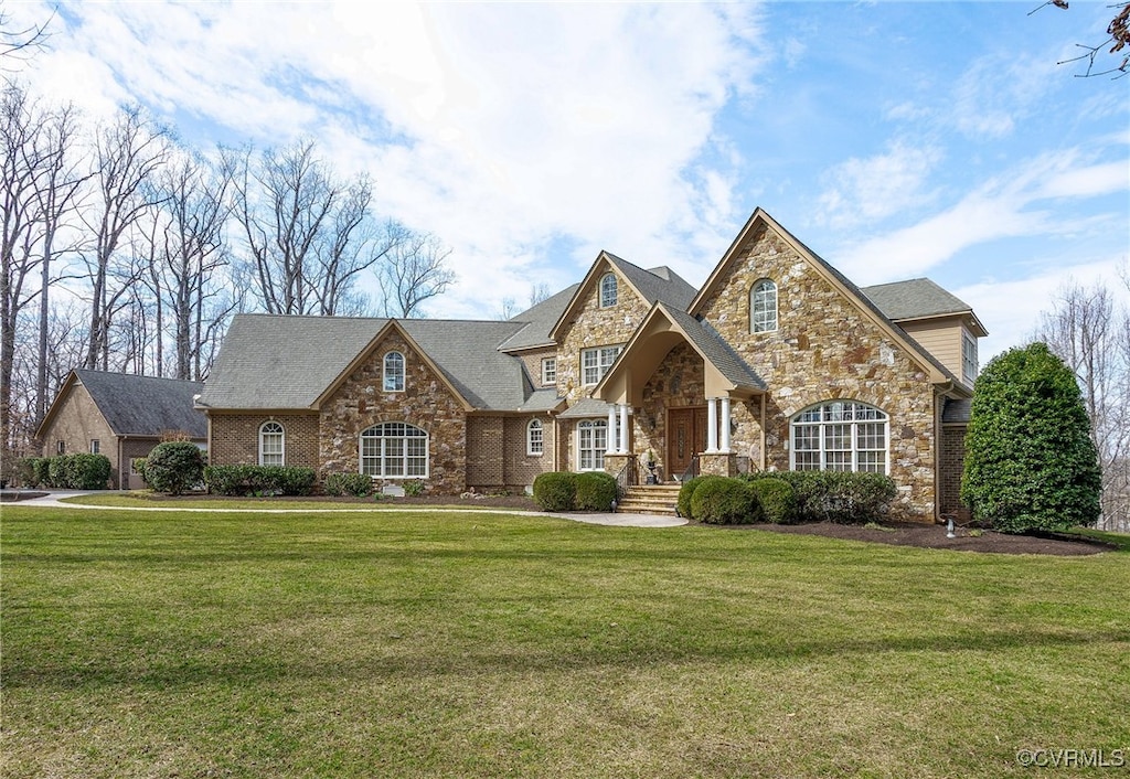 french country style house featuring stone siding and a front yard