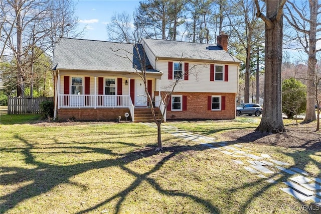 split level home featuring brick siding, a chimney, a shingled roof, covered porch, and a front lawn