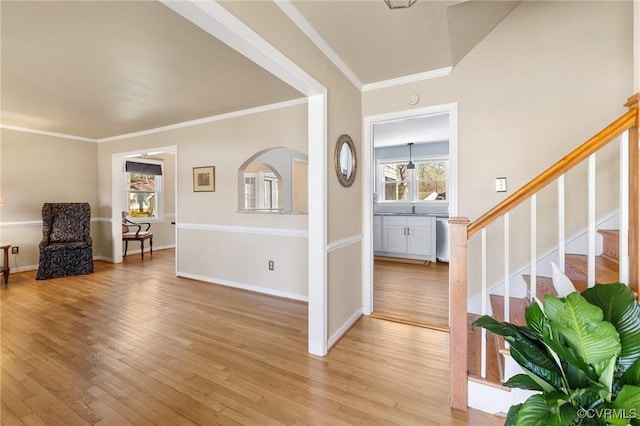 interior space with arched walkways, baseboards, stairs, ornamental molding, and light wood finished floors