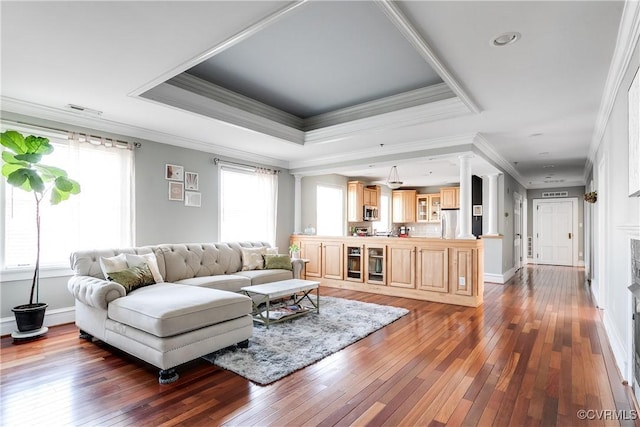 living area with decorative columns, baseboards, a raised ceiling, and dark wood finished floors