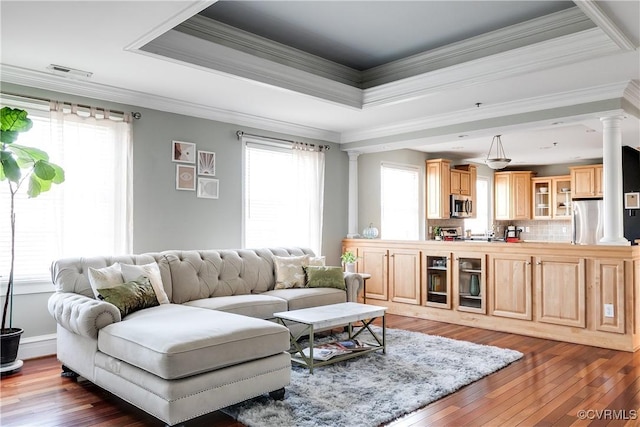 living room with a healthy amount of sunlight, ornate columns, and a raised ceiling