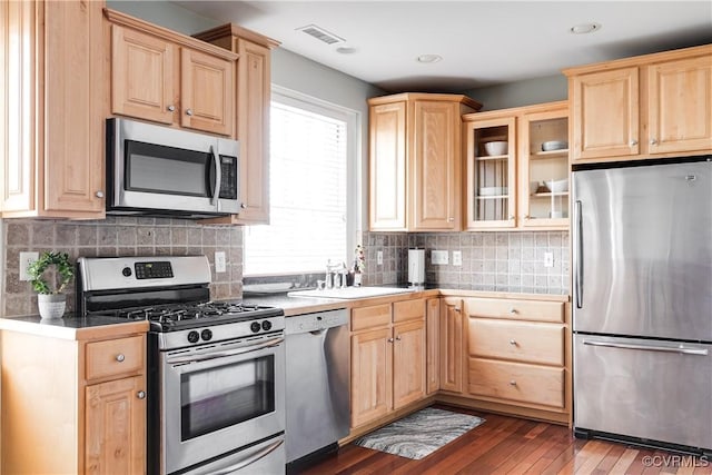 kitchen with visible vents, appliances with stainless steel finishes, light brown cabinetry, dark countertops, and glass insert cabinets