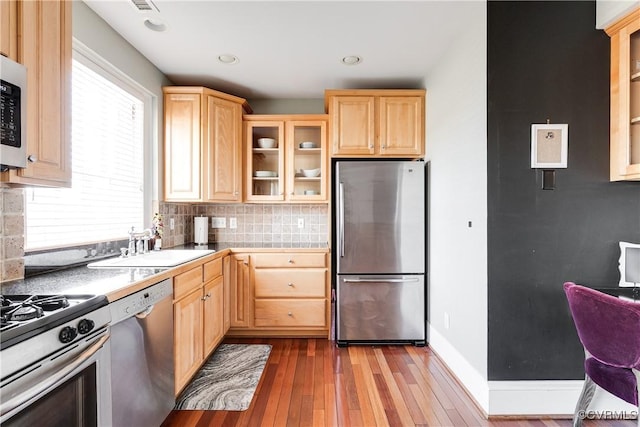 kitchen with light brown cabinetry, appliances with stainless steel finishes, a sink, and glass insert cabinets