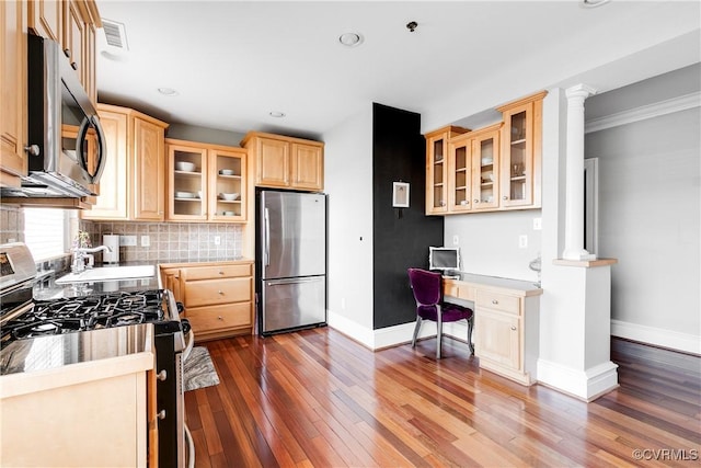 kitchen featuring appliances with stainless steel finishes, built in study area, light brown cabinetry, tasteful backsplash, and glass insert cabinets