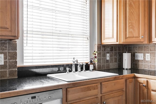 kitchen with brown cabinets, dark countertops, decorative backsplash, a sink, and dishwashing machine